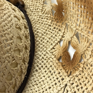 Dettaglio di un cappello di paglia beige con trama traforata e decorazione di perle in legno