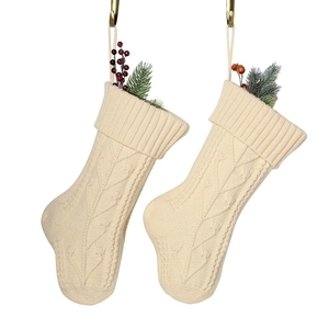 Pair of beige cable knit Christmas stockings with artificial pine branches and red berries