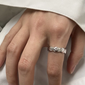 Minimalist silver ring with diamond-shaped woven texture on a hand with white shirt cuff