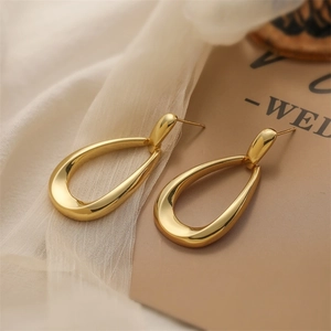 Macro shot of large polished gold water drop earrings on a white and brown fabric backdrop