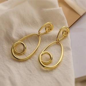 Detailed close-up of golden hollow teardrop earrings on minimalist linen background
