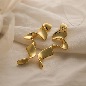 Close-up of golden wavy fluid design earrings on soft fabric with sculpted metal detail