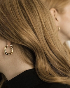 Close-up of model wearing chunky golden C-shaped hoop earrings with a polished finish