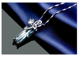 Detail of a square blue crystal pendant with silver chain on blue silk background