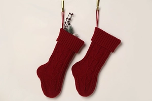 Pair of red cable-knit Christmas stockings with berry branches on a gold wall hook