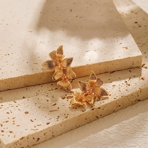 Artistic gold-plated double floral earrings displayed on elegant beige stone steps