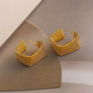 Close-up of golden square hoop earrings with textured brushed finish and geometric design