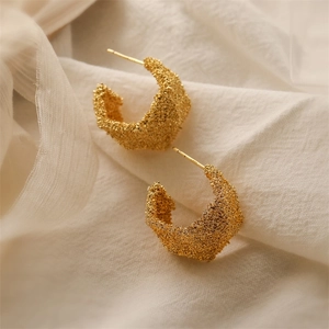 Macro shot of gold chunky hoop earrings with irregular lava texture on white silk fabric