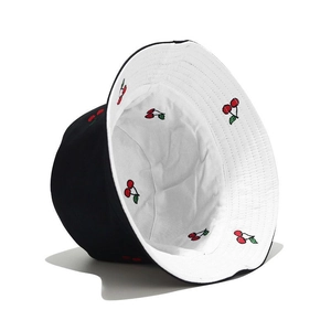 Detail of reversible bucket hat featuring red cherry embroidery on black and white sides