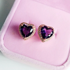 Macro view of heart-shaped purple crystal earrings with white zircon on pink velvet box