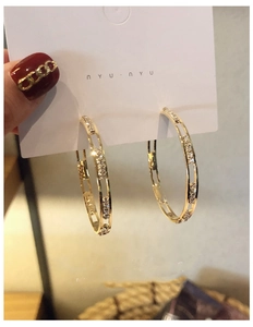 Close-up of gold C-shaped hoop earrings with clear rhinestones and hollow metal design