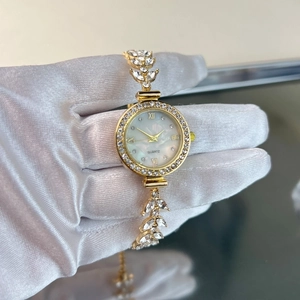 Detail of gold quartz watch featuring leaf-shaped crystal bracelet and mother of pearl dial