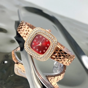 Detail of a rose gold square watch with a red dial and diamond markers on a reflective surface