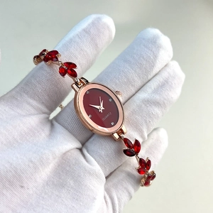 Detail view of oval gold watch with red dial and crystal leaf-shaped bracelet