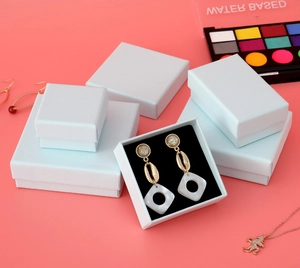 Stack of white textured cardboard jewelry gift boxes in various sizes on pink background