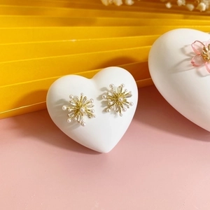 Star-shaped golden stud earrings with white pearls and zircons on heart display stand