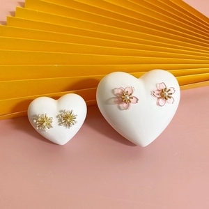 Pink cherry blossom and golden snowflake stud earrings on heart-shaped display stands