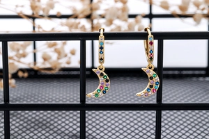Detail of moon-shaped gold earring with multicolored cubic zirconia on a black stand