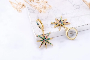 Detail of gold star drop earrings with multi-color zircon stones on marble