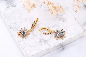 Close-up of golden starburst earrings with multi-color zircon stones on marble texture