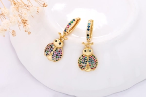 Macro shot of gold ladybug earrings with colorful zircon inlay on a white plate