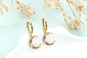 Macro shot of gold moon huggie earrings with colorful zircon stones on a white stand