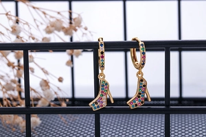 Detail of gold stiletto heel drop earrings with multicolor cubic zirconia on a black grid