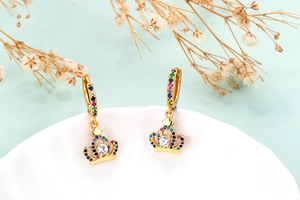 Detail view of golden crown hoop earrings with colorful cubic zirconia on a white plate