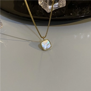 Detailed view of square gold necklace pendant with white mother of pearl inlay