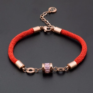 Detail of red braided cord bracelet with rose gold clasp and pink crystal charm