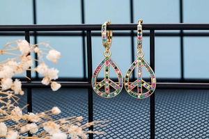 Detail of gold hoop earrings with teardrop peace sign pendants and colorful crystals