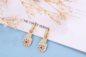 Detail of golden Hamsa Hand earrings with pink heart stones and pavé set cubic zirconia