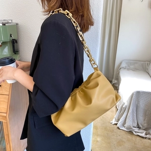 Fashionable yellow cloud bag with chunky gold chain strap worn by a model in a cafe