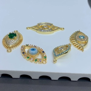 Five gold-plated evil eye charms with colorful crystals on a textured white surface
