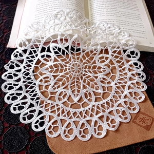 Close-up of white round lace coaster with intricate floral hollow patterns on a book