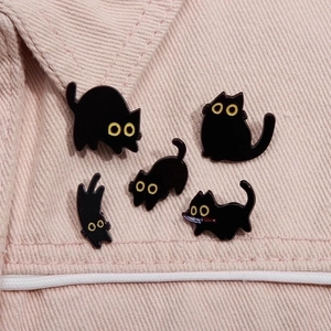 Cinco bonitos pines de esmalte de gato negro en varias poses sobre tela vaquera rosa