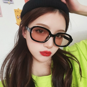 Close-up of model wearing black oval thick-frame sunglasses with vibrant red lenses
