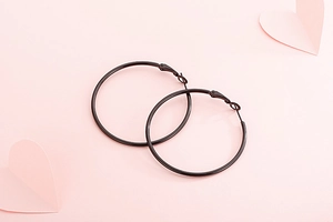 Gros plan de grandes créoles en acier inoxydable noir mat sur fond rose doux