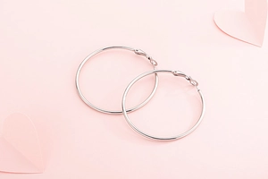 Créoles en acier inoxydable argenté sur fond rose avec décorations en forme de cœur