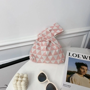 Close-up of pink and white geometric triangle knit wrist bag with minimalist accessories