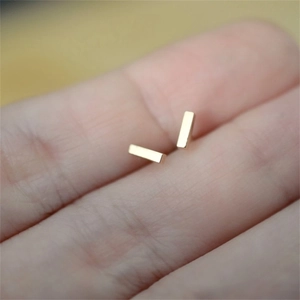 Macro view of minimalist gold bar earrings on fingertip showing polished mirror finish