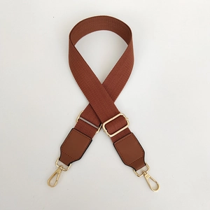 Detail of dark brown canvas bag strap with golden metal hooks and adjustable buckle