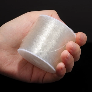 Hand holding a roll of clear elastic beading cord for DIY jewelry making and crafts