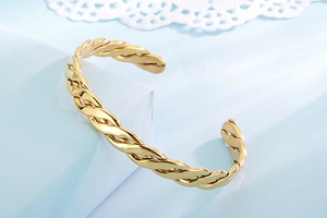Macro detail of twisted golden stainless steel braided cuff bracelet on blue background