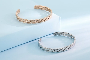 Detailed view of twisted cable metal bangles in rose gold and silver on geometric blocks