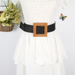 Detail view of a black woven straw belt with a square wooden buckle on a white dress