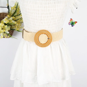 Detail of beige woven straw belt with a round rattan buckle on a white summer dress
