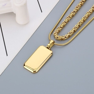 Detailed macro shot of gold double-layer necklace with dog tag pendant on grey background