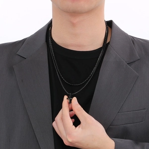 Close-up of a man wearing a double-layer black cross pendant necklace with a Cuban chain