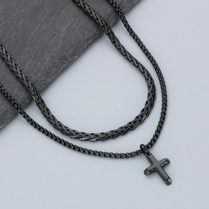 Detail of a black layered cuban chain necklace with a cross pendant on a stone surface